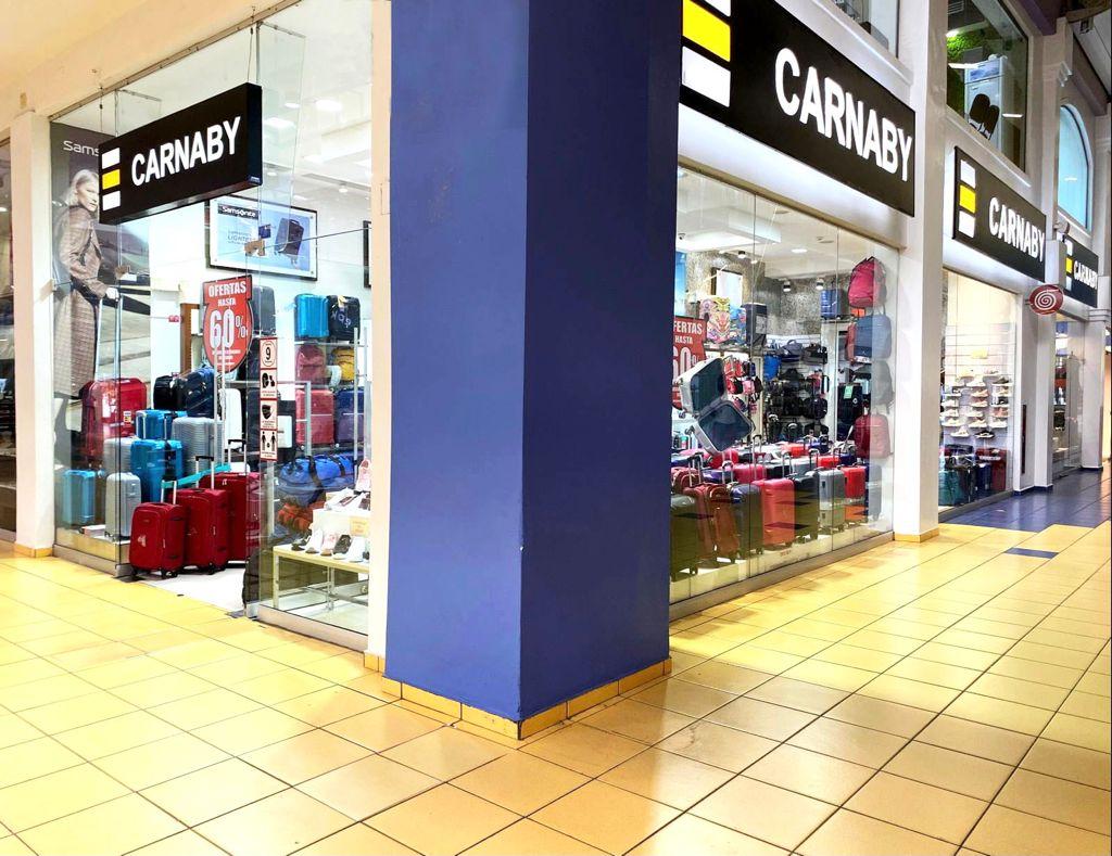 Fachada de Carnaby en Albrook Mall, con rótulos negros y amarillos y maletas en los escaparates.